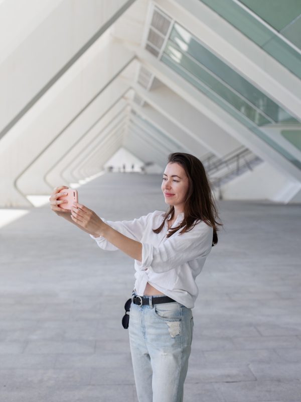 Young woman using mobile phone video chatting on social media in modern architecture near office
