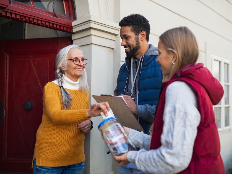 Young door to door fundraisers talking to senior woman and collecting money for charity in street