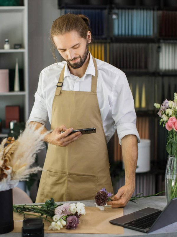 Florists making bouquet of flowers on counter and taking photo on smartphone for social media.