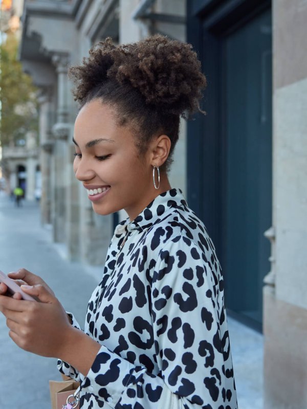 Happy carefree curly haired pretty teenager enjoys positive network messaging in social media holds