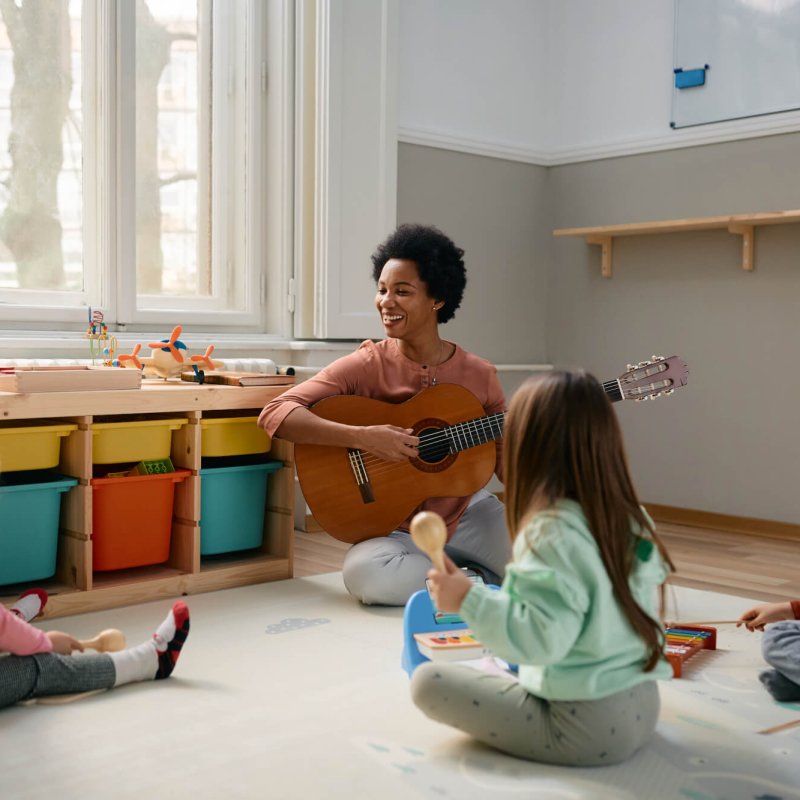 Happy black teacher and group of kids enjoying during music class at kindergarten.