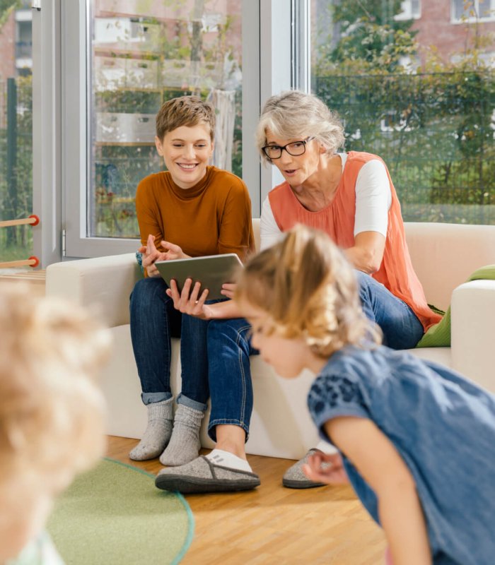 Pre-school teachers with tablet looking at children in kindergarten