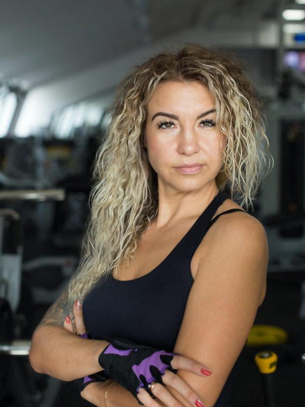 woman-with-long-blonde-curly-hair-portrait-of-a-fitness-trainer-in-the-gym