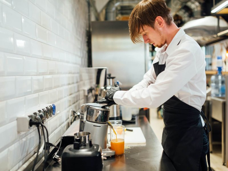 A cafe worker makes orange juice in a juicer. Catering kitchen work.