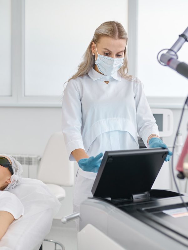 Cosmetologist working on laser machine adjusting mode for patient treatment