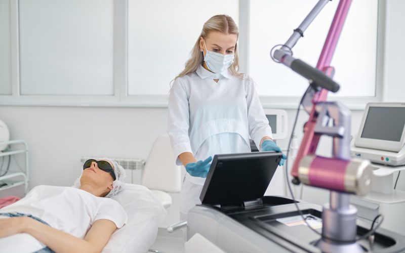 Cosmetologist working on laser machine adjusting mode for patient treatment